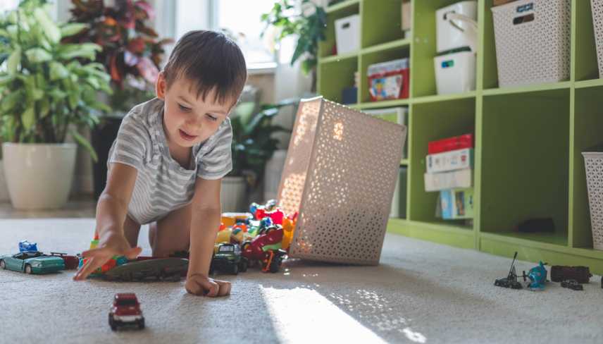 A cheerful European boy plays with colorful cars on the carpet in his room. 